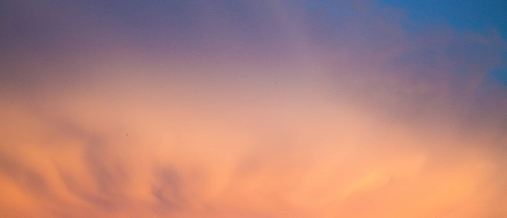A plane flying over a colorful sky at sunset.